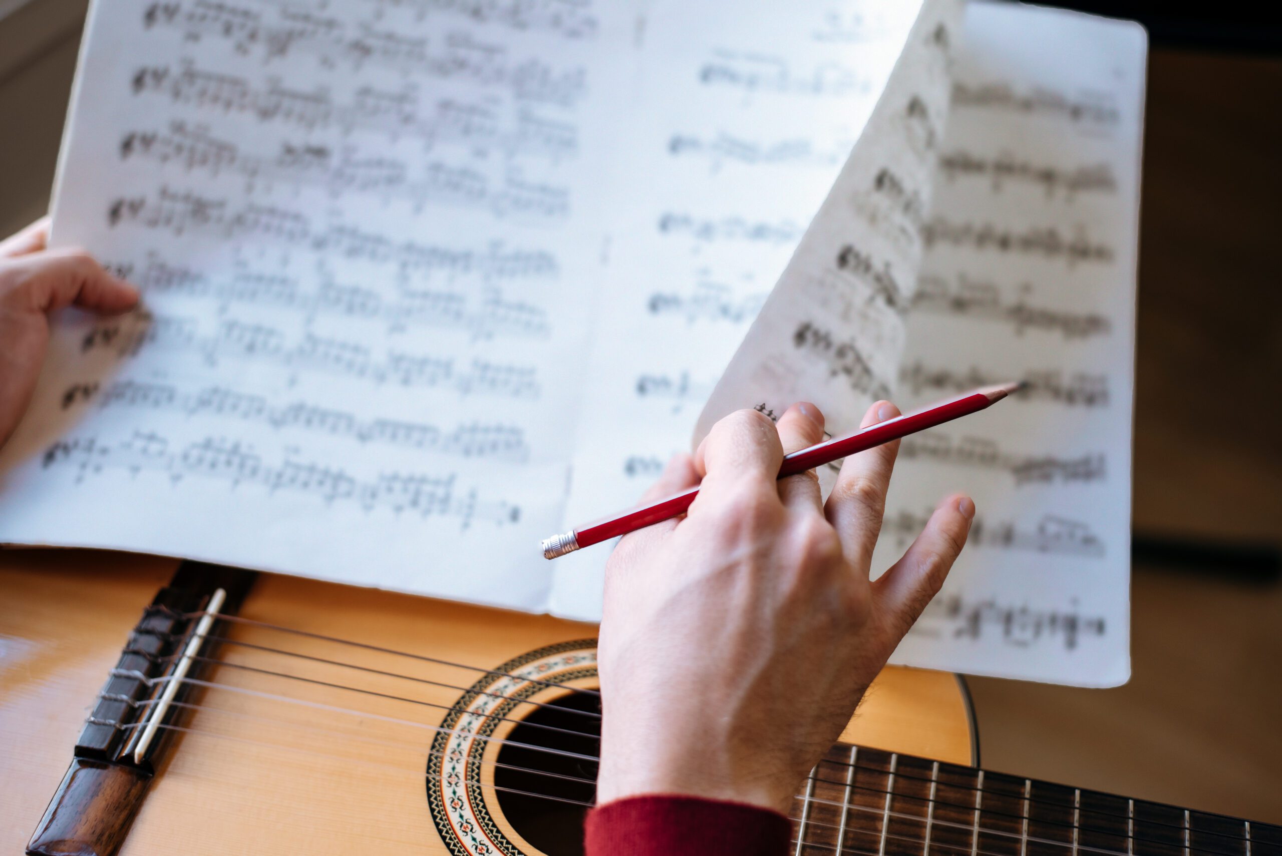Man hands with sheet music playing guitar Crop man hands with sheet music playing guitar during rehearsal in studio.